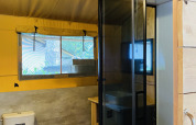 Baño en tiendas safari con inodoro, ducha y ventana en Familiepark Goolderheide, Bélgica.