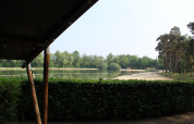 Vista desde una tienda safari con sanitario en Familiepark Goolderheide, Bélgica, hacia lago y bosque.