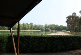 Vista desde una tienda safari con sanitario en Familiepark Goolderheide, Bélgica, hacia lago y bosque.