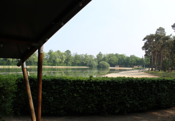 Vista desde una tienda safari con sanitario en Familiepark Goolderheide, Bélgica, hacia lago y bosque.