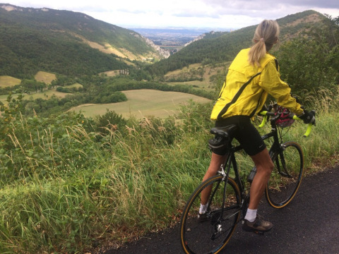 Ciclista con chaqueta amarilla admira el paisaje montañoso en Camping Le Gallo Romain, Auvernia-Ródano-Alpes, Francia.