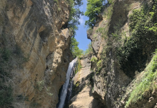 Cascata che scende fra le rocce e alberi verdi a Camping Le Gallo Romain in Auvergne-Rhône-Alpes, Francia.
