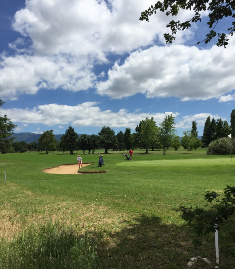 Dos personas juegan al golf en un campo verde bajo un cielo parcialmente nublado en Camping Le Gallo Romain, Francia.