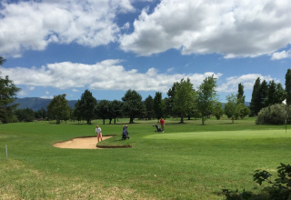 To personer spiller golf på en grøn bane under en blå himmel med skyer i Camping Le Gallo Romain, Frankrig.