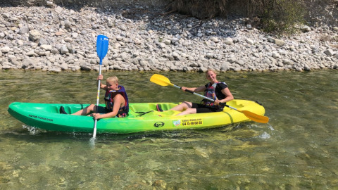 Dos personas remando en un kayak verde y amarillo en un río claro en Camping Le Gallo Romain, Francia.