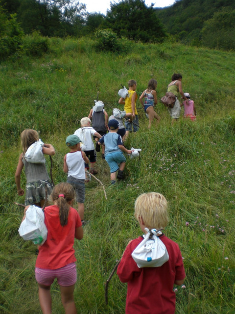 Un grupo de niños sube una colina verde junto a un adulto en Camping Le Gallo Romain, Auvernia-Ródano-Alpes.