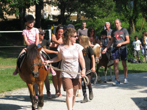 Niños montando ponis acompañados por adultos en Camping Le Gallo Romain en Auvernia-Ródano-Alpes, Francia.