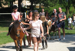 Børn rider på ponyer med voksne guider ved Camping Le Gallo Romain, Auvergne-Rhône-Alpes, Frankrig.