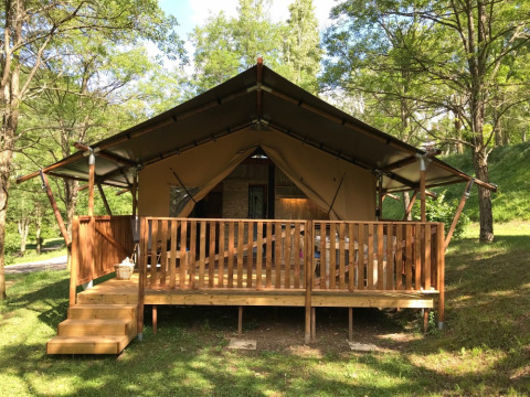 Tienda safari con instalaciones sanitarias en Camping Le Gallo Romain en Francia, rodeada de árboles verdes.