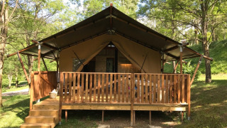 Tienda safari con instalaciones sanitarias en Camping Le Gallo Romain en Francia, rodeada de árboles verdes.
