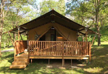 Tienda safari con instalaciones sanitarias en Camping Le Gallo Romain en Francia, rodeada de árboles verdes.