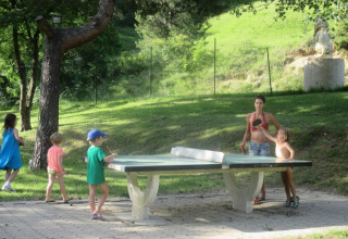 Børn og voksne spiller bordtennis på udendørs bord i Camping Le Gallo Romain, Auvergne-Rhône-Alpes, Frankrig.
