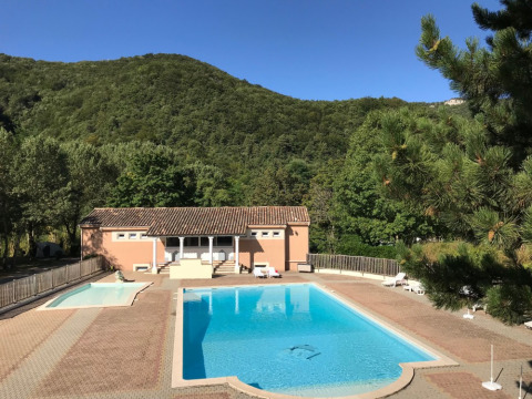 Piscina y cabaña vacacional en Camping Le Gallo Romain, rodeadas de colinas verdes en Auvergne-Rhône-Alpes.