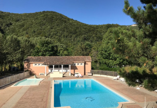 Swimmingpool og feriebolig ved Camping Le Gallo Romain, omgivet af grønne bjerge i Auvergne-Rhône-Alpes.