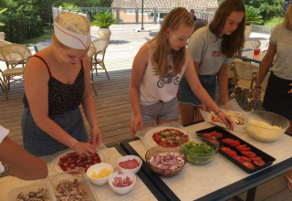 Teenagere laver pizzaer sammen udendørs på Camping Le Gallo Romain i Auvergne-Rhône-Alpes, Frankrig.