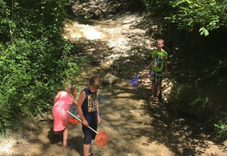 Bambini che giocano in un piccolo ruscello tra gli alberi al Camping Le Gallo Romain in Alvernia-Rodano-Alpi.