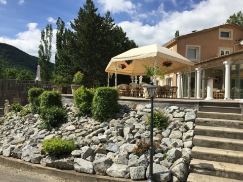 Terraza soleada con zona de estar cubierta, plantas de jardín y rocalla en Camping Le Gallo Romain, Francia.