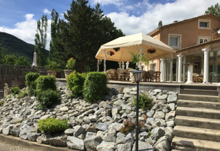 Solrig terrasse med udendørs siddeområde, haveplanter og stenvæg ved ferieparken Camping Le Gallo Romain.