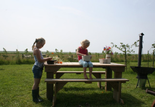 To børn leger ved et picnicbord på en græsplæne i solskin på Feather Down De Zeekraal Terschelling, Friesland.