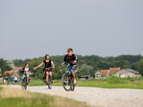 Tres personas andan en bicicleta por un camino de grava cerca de Oosterend, Frisia, Países Bajos, rodeados de campo.