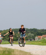 Tres personas andan en bicicleta por un camino de grava cerca de Oosterend, Frisia, Países Bajos, rodeados de campo.