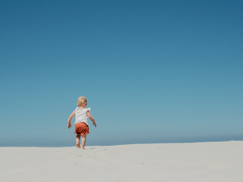 Un jeune enfant marche sur une dune de sable sous un ciel bleu à Feather Down De Zeekraal Terschelling, Friesland.
