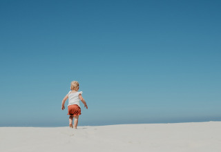 A small child walks on a sandy hill under clear blue sky at Feather Down De Zeekraal Terschelling, Friesland.