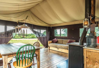 Interior de una tienda glamping con suelo de madera, mesa de comedor, sofá y estufa en un parque vacacional.