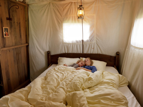Madre e hijo descansan juntos en una cama acogedora dentro de una tienda glamping en un parque vacacional.