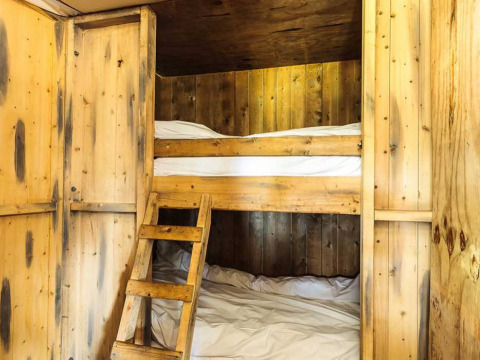 Vista interior de una cabaña glamping con literas de madera y paredes de madera, ambiente acogedor y rústico.
