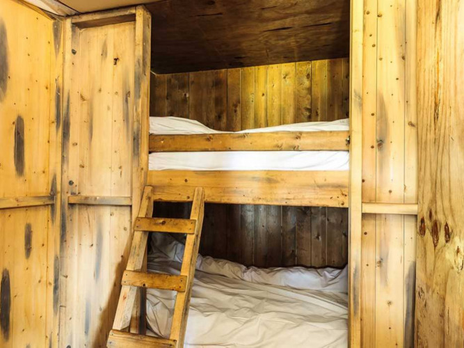 Binnenaanzicht van een glampingverblijf met houten stapelbedden en een knusse, rustieke houten wand.
