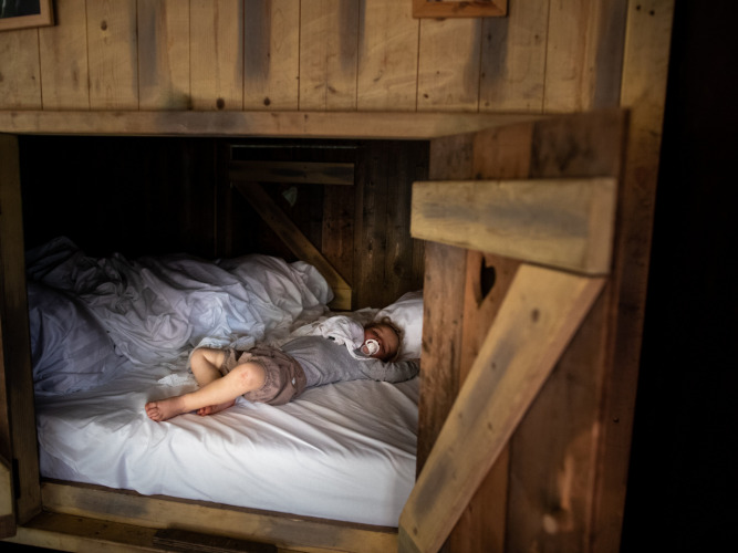 Een kind ligt in een knus houten bed en drinkt melk bij een glamping-accommodatie in een vakantiepark.