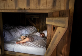 A child lies in a cozy wooden bed, drinking milk at a glamping accommodation in a holiday park.