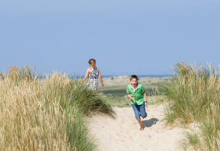 Zwei Kinder spielen an den Dünen bei Oosterend in Friesland, Niederlande, mit Meerblick und blauem Himmel.