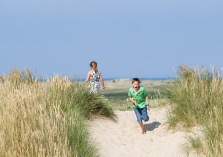 Twee kinderen spelen in de duinen bij Oosterend, Friesland, Nederland, met uitzicht op zee en blauwe lucht.