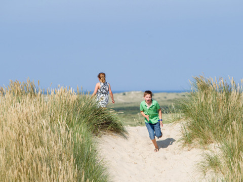 Due bambini giocano tra le dune vicino a Oosterend, Frisia, Paesi Bassi, con il mare sullo sfondo.