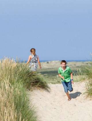 Dos niños juegan entre las dunas cerca de Oosterend, Friesland, Países Bajos, con el mar y cielo azul al fondo.