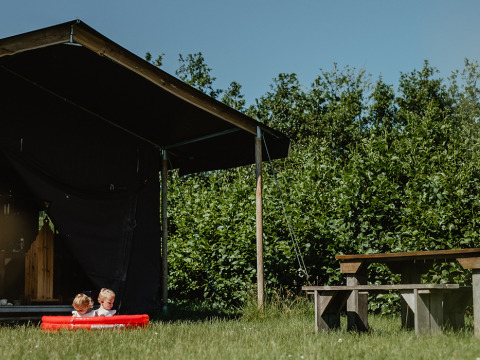 Twee kinderen spelen in een klein zwembadje bij een tent op Feather Down De Zeekraal Terschelling, Friesland, Nederland.