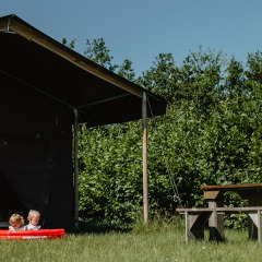 Dos niños juegan en una pequeña piscina junto a una tienda en Feather Down De Zeekraal Terschelling, Frisia, Países Bajos.