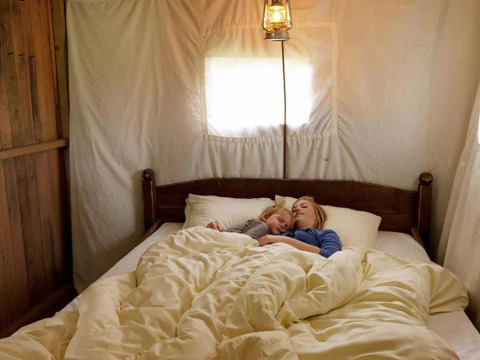 Dos personas duermen en una cama acogedora dentro de una tienda, alojamiento glamping en parque vacacional.