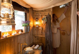 Salle de bain chaleureuse en glamping avec murs en bois, bougies, lanternes et femme en peignoir.