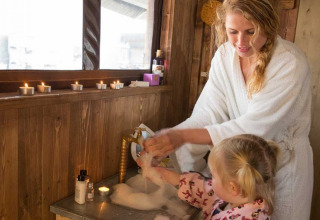 Mutter und Kind im Bademantel waschen Hände an einem Waschbecken im Glamping-Holzhaus mit Kerzen.