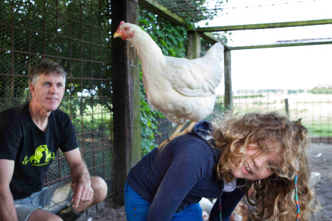 Man en kind bij een vakantieboerderij in Friesland, Nederland, met een witte kip op de rug van het kind.