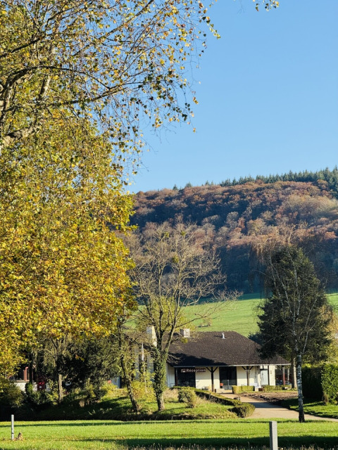 De receptie van Camp Diekirch in Luxemburg, omringd door bomen, gras en een heuvelachtig herfstlandschap.