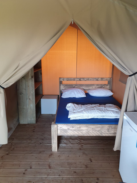 Binnenzijde van een safaritent op Camp Diekirch in Luxemburg met bed, rekken en koelkast.