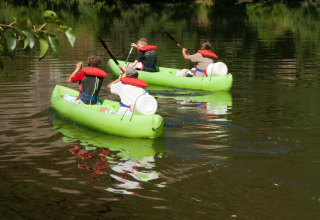 To grønne kanoer på en sø ved Camping lac Aux Oiseaux i Occitanie, Frankrig, med fire personer ombord.