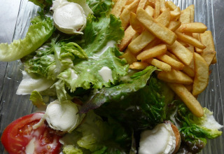 En tallerken med pommes frites, grøn salat, tomatskiver og gedeost serveret på Camping lac Aux Oiseaux, Occitanie.