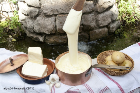 Aligot francés servido al aire libre con patatas, mantequilla, ajo y una olla de cobre sobre un mantel.