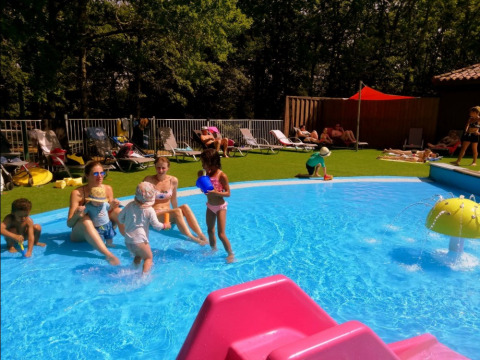 Niños y adultos disfrutan de un día soleado junto a la piscina en Camping lac Aux Oiseaux, Occitanie, Francia.