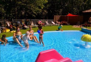 Børn og voksne nyder en solrig dag ved poolen på Camping lac Aux Oiseaux feriepark i Occitanie, Frankrig.